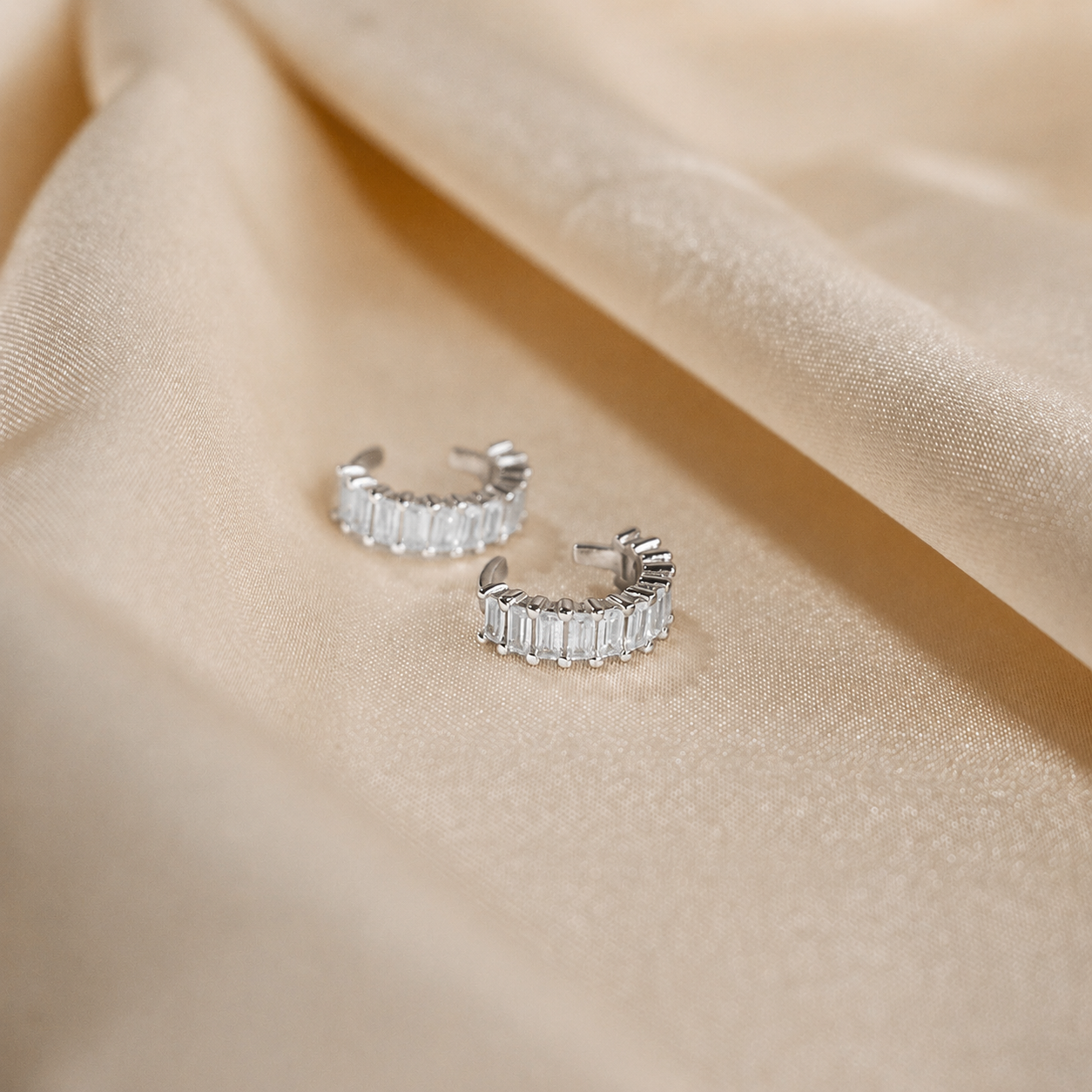 Silver hoop earrings with clear gemstones on a beige fabric background